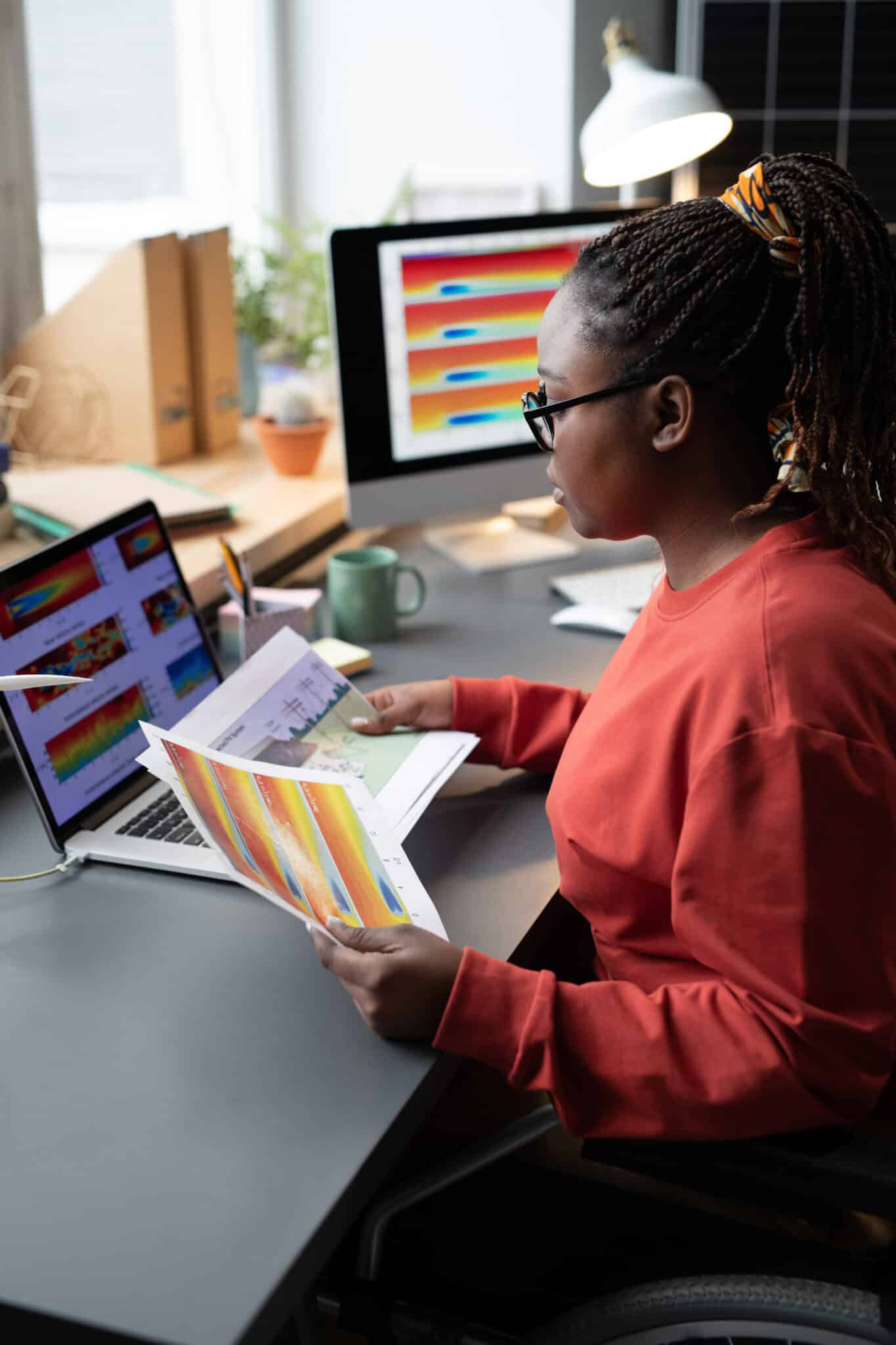 African businesswoman with disability examining the graphs on papers during her work at the table with laptop